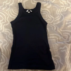 Svart ribbad linnetopp - En svart, ribbad linnetopp med sportig skärning och breda axelband. Perfekt för lager-på-lager eller att bära som den är. Enkel och stilren design som funkar till många olika looks.