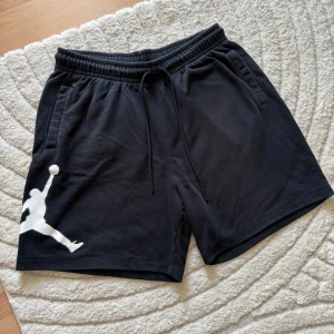 Jordan svarta shorts med logga XL - Svarta Jordan shorts i mjuk bomull med klassisk vit Jumpman-logga på vänster ben. Elastisk midja med snörning och två sidofickor. Perfekta för sport eller chill, riktigt clean look och skön passform.