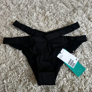 Svarta bikiniunderdelar från H&M - Svart bikiniunderdel från H&M med trendig dubbla midjeband som korsar framtill. 
