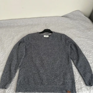 Grå stickad tröja Tom Tailor L - Säljer en gråmelerad stickad tröja från Tom Tailor i storlek L. Tröjan har rund halsringning, lång ärm och en snygg ribbad kant nedtill. Perfekt för dig som gillar en enkel men stilren look till höst och vinter. Tröjan passar som M också