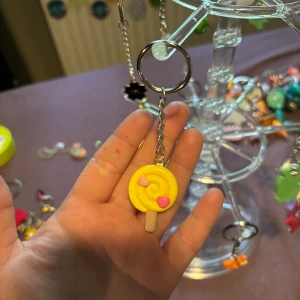 Nyckelring med gul klubba och hjärtan - Söt nyckelring med en gul klubba i spiralform och två små hjärtan i rosa och rött. Perfekt accessoar för att piffa upp väskan eller nyckelknippan. Klubban har en glansig finish och detaljer i pastellfärger.