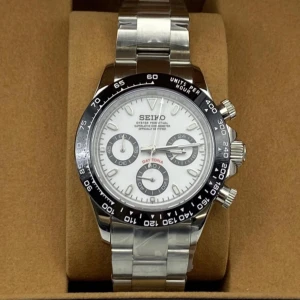 Seiko Daytona-inspirerad klocka silver - Stilren Seiko klocka med silverfärgad länk i metall och vit urtavla. Klockan har svart bezel med tachymeter, tre subdials och tydliga indexmarkeringar. Kronograffunktion och sportig design som sticker ut på handleden.