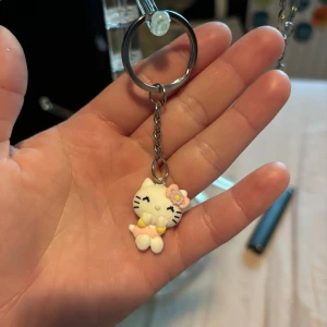 Hello Kitty nyckelring med blomma - Supergullig Hello Kitty nyckelring med en vit katt som har en rosa blomma på huvudet och en söt gul rosett. Perfekt att hänga på väskan eller nycklarna för en extra söt detalj.