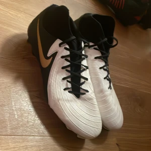 Nike svartvita fotbollsskor - Snygga fotbollsskor från Nike i svart och vitt med guldigt swoosh på sidan. Skorna är i väldigt bra skick, den säljs för den passar inte mig längre och kan mötas inom stockholm