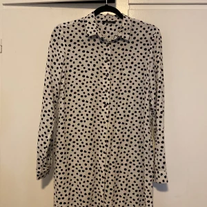 Prickig skjortklänning från Esmara - Vit skjortklänning med svarta prickar från Esmara. Långärmad med klassisk krage och knäppning framtill. Lätt och flowy känsla, perfekt för dig som gillar en avslappnad men ändå snygg look.