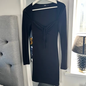 Svart klänning från BikBok - Snygg svart klänning från BikBok i storlek XS. Klänningen har långa ärmar och en knytning framtill som ger en fin detalj💕