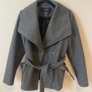 Grå kappa från Vero Moda - Snygg grå kappa från Vero Moda med bred krage och knytbälte i midjan. Använts fåtal gånger, ingen tecken på användning!!🥰 