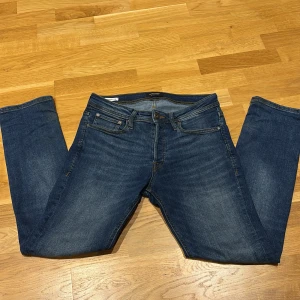 Blå jeans från Jack & Jones - Snygga blå jeans från Jack & Jones med klassisk femficksdesign och knappgylf. Perfekta för en avslappnad stil. Märkeslapp i läder baktill.