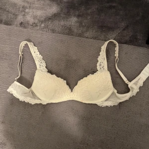 Vit spets-bh - Säljer en elegant vit bh med vacker spetsdetalj från intimissimi. Bh:n har justerbara axelband och en mjuk kupa med push up för extra komfort. Perfekt för att känna sig både bekväm och stilfull.Storlek 75b använd en gång säljes då en var för liten. Nypris 500 kr mitt pris 370 kr
