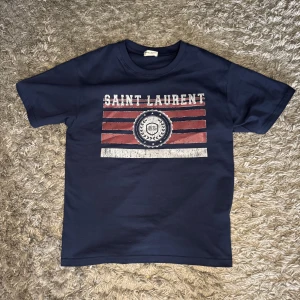 Saint Laurent tröja - Snygg unik sait Laurent t- shirt som är helt perfekt till sommaren och som matchar med precis allt. Den är i använt skick men syns verkligen inte. Skriv vid frågor och funderingar :)