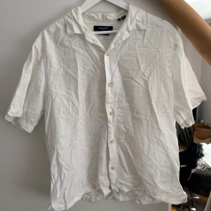Vit kortärmad skjorta från Jack & Jones - Säljer en stilren vit skjorta från Jack & Jones i storlek M. Skjortan är kortärmad och har knappar framtill. Perfekt för en avslappnad och snygg look.