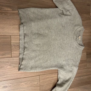 Grå stickad tröja från Gina Tricot - Säljer en stilren grå stickad tröja från Gina Tricot. Tröjan har en klassisk rund hals och ribbade detaljer vid ärmslut och nederkant. Perfekt för kyligare dagar. Lite missfärgad i ärmarna!!! Pris kan diskuteras!!!