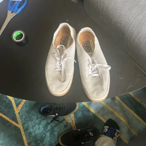 Vita sneakers från Vans - Säljer ett par vita sneakers från Vans med snörning och rund tå. Skorna har en stilren design och är perfekta för en avslappnad stil. De är tillverkade i ett syntetmaterial med en bekväm innersula av kork.