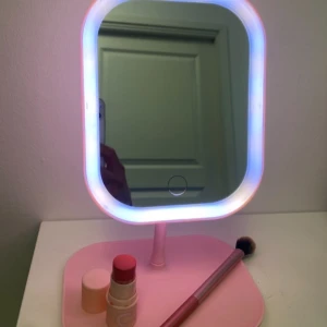 Rosa sminkspegel med LED-belysning - Snygg rosa sminkspegel med inbyggd LED-belysning för perfekt sminkapplikation. Spegeln står på en stabil bas och har en touch-knapp för att justera ljuset. Perfekt för att få till den där perfekta looken varje gång!19x23