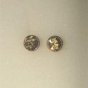 Guldiga örhängen med glittriga stenar - Säljer ett par eleganta guldiga örhängen med glittriga stenar. Perfekta för att ge en touch av glamour till din outfit. De är små och diskreta men ändå iögonfallande.