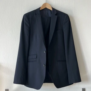 Svart/Blå kostym från Riley - Elegant svart kostym från Riley i slim fit. Kavajen har två knappar och klassiska fickor. Perfekt för formella tillfällen.