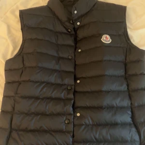 Svart dunväst från Moncler - Säljer en snygg äkta marinblå väst från Moncler. Västen har en klassisk design med knappar framtill och Monclers logga på bröstet. Perfekt för kyligare dagar när du vill hålla stilen. Använd 2 gånger och jag säljer eftersom den inte kommer till användning. 