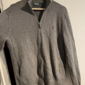 Polo Ralph Lauren tröja - Säljer en stilren grå helzip Polo Ralph Lauren tröja/cardigan i mycket fint skick. Storlek M. Har inte använt den mycket alls på grund av att den är för stor för mig. Pris går att diskuteras. Jag är 180 cm ungefär. Bara att höra av sig vid frågor och funderingar!