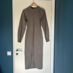 Grå stickad långklänning - Säljer en stilren grå stickad långklänning med långa ärmar och ribbad halsringning. Perfekt för kyligare dagar och ger en mysig känsla. Passar bra till både vardag och mer uppklädda tillfällen.