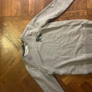 Grå sweatshirt från Scotch & Soda - Säljer en stilren grå sweatshirt från Scotch & Soda med ett diskret tryck på bröstet. Tröjan har långa ärmar och en rund halsringning. Perfekt för en avslappnad look.