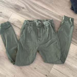 Gröna byxor från Zara - Säljer ett par gröna byxor från Zara med elastisk midja och knappdetalj. Perfekta för en avslappnad stil. *barnsize