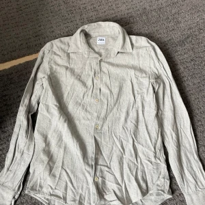 Grå skjorta från Zara - Säljer en stilren grå skjorta från Zara i storlek M. Skjortan har långa ärmar och knappar framtill. Perfekt för en klassisk look.