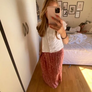 Röd mönstrad långkjol - Säljer en röd långkjol med ett vackert mönster. Kjolen har en bekväm passform och är perfekt för varma dagar. Den är lätt och luftig, vilket gör den idealisk för sommarens alla äventyr. 