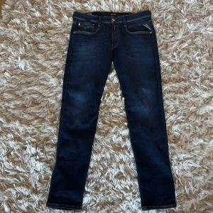 Replay Anbass 33/32  - Snygga mörkblå jeans från Replay i modellen Anbass. De har en slim fit och klassisk femficksdesign med snygga detaljer på bakfickorna. Perfekta för en stilren look.