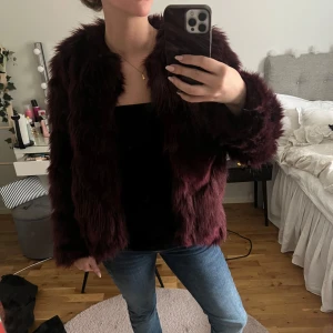 Vinröd pälsjacka - Säljer en snygg vinröd pälsjacka med långärmad design. Jackan har en lyxig känsla och är perfekt för att hålla sig varm och stilren under kyligare dagar. Passar bra till både jeans och klänning.