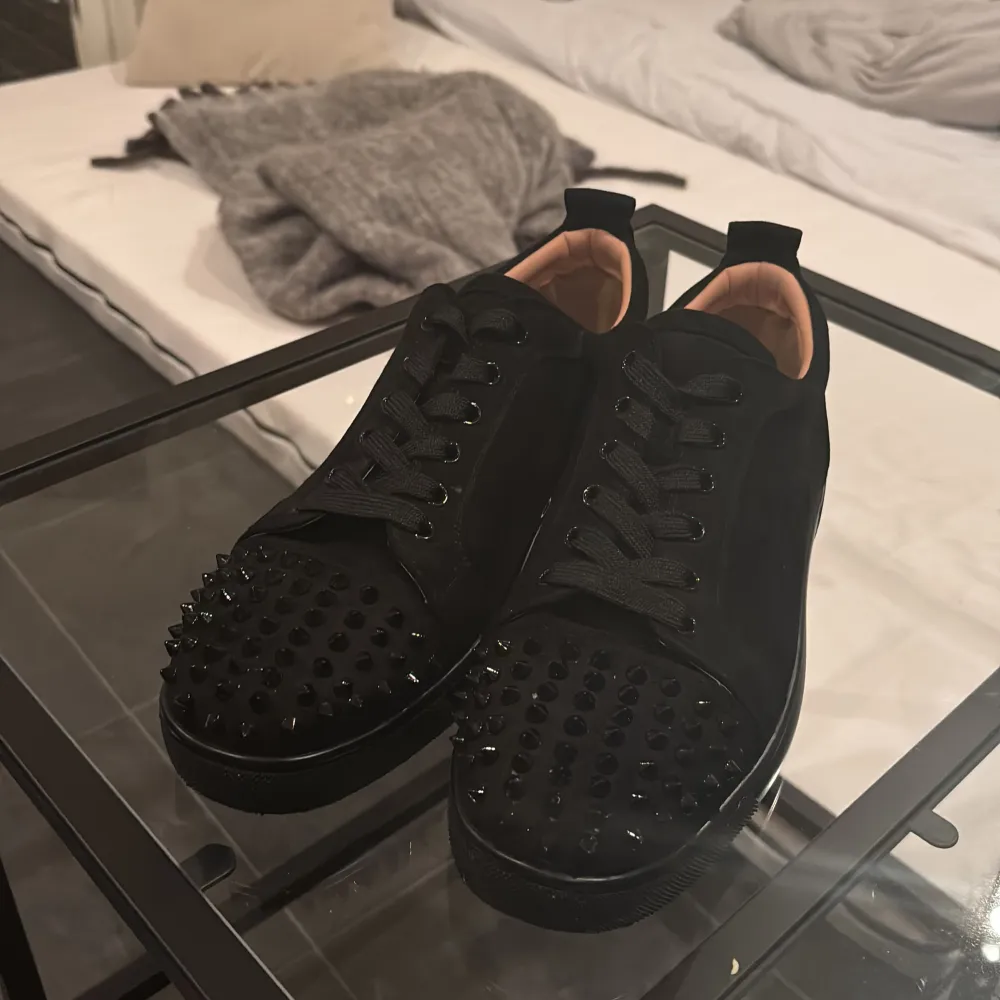 Snygga svarta sneakers från Christian Louboutin med ikoniska röda sulor och nitar på tån. Skorna har en snörning och är tillverkade i skinn, vilket ger skon en lyxig känsla. Perfekt för att ge din outfit en edgy touch. En nit fattas men de syns inte . Kengät.