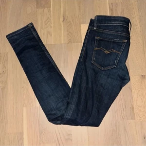 Mörkblå jeans från Replay - Snygga mörkblå jeans från Replay med klassisk femficksdesign och guldfärgade sömmar. Jeansen har en knappgylf och en liten logga på bakfickan. Perfekta för en stilren look.
