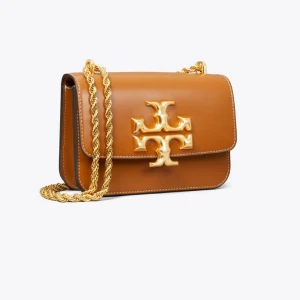 Tory Burch väska  - Snygg brun axelväska med en elegant guldkedja och ett stort guldfärgat emblem på framsidan. Väskan har en praktisk dragkedja inuti för extra säkerhet. Perfekt för att ge en touch av lyx till din outfit. Märket är Tory Burch i modellen Eleanor och var köpt för 8000kr. Väskan är äkta och dustbag kommer också med