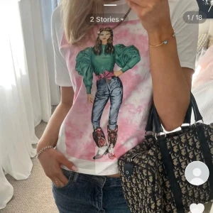 Vit t-shirt med tryck - Snygg vit t-shirt med ett färgglatt tryck av en kvinna i gröna puffärmar och jeans. Perfekt för en avslappnad stil med en touch av konstnärlig flair.