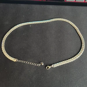 Silverfärgat halsband - Elegant silverfärgat halsband med en klassisk kedjedesign. Perfekt för att lägga till en touch av stil till din outfit. Halsbandet har en justerbar kedja med ett enkelt lås för att passa olika längder.