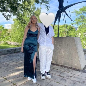 Mörkgrön sidenklänning med slits - Elegant mörkgrön klänning i siden med smala axelband och en stilren slits framtill. Klänningen har en figurnära passform som framhäver silhuetten. Öppen i ryggen och även fin där! Använd på balen 1gång å sen har den hängt i garderoben så den är som ny! Skriv för mer info eller bilder:) köparen står för frakten! Köptes för 1000kr