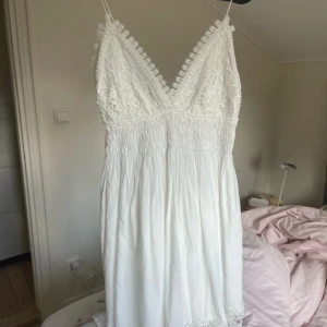 Vit spetsklänning med v-ringning - Säljer en vacker vit klänning med spetsdetaljer och v-ringning. Den är från Zara och är perfekt till sommaren! Endast använd 1 gång