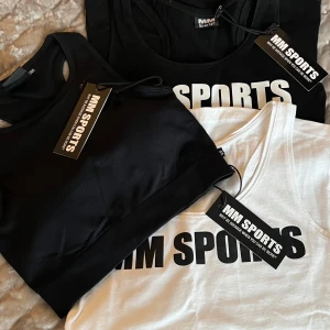 Svart och vit linnetopp och sportbehå  från MM Sports - Säljer snygga och bekväma linnetoppar från MM Sports i svart och vitt. Perfekta för träning med en stilren design och tryck framtill. Linnet har en tight passform och ärmlös design som ger rörelsefrihet.