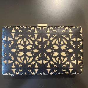 Svart och beige kuvertväska från Blanco Suite - Elegant kuvertväska/clutch i svart och beige. Väskan har en metallram och en kedja för att bäras över axeln. I nyskick 