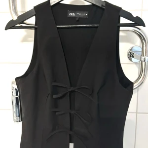 Svart väst från Zara - Riktigt snygg svart väst från Zara med knytning framtill. Västen är v-ringad och är perfekt för festliga tillfällen. 