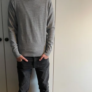 Grå merinoullströja från Uniqlo - Säljer en stilren grå tröja från Uniqlo. Den är långärmad och har en klassisk rund halsringning. Perfekt för en minimalistisk look. Tröjan är tillverkad i ett mjukt material som känns skönt mot huden. Storleken är XS!