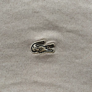 Beige pikétröja från Lacoste - Säljer en stilren beige pikétröja från Lacoste med klassisk krage och knappar framtill. Tröjan har det ikoniska krokodilemblem på bröstet. Perfekt för en avslappnad och snygg look.
