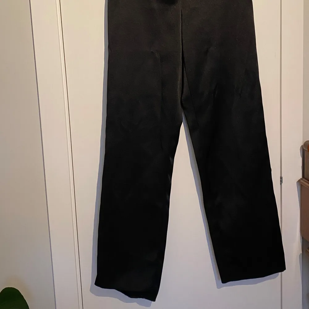 Snygga svarta kostymbyxor från H&M med hög midja och raka ben. Byxorna har en stilren design med diskreta fickor baktill och stängs med dragkedja och knapp framtill. Perfekta för en elegant look. Ena fållen släppt på ena benet, men enkelt att åtgärda. . Farkut & Housut.