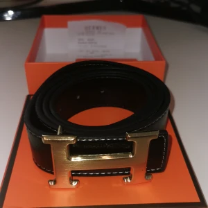 Svart bälte med guld H - Snyggt skarpt bälte. Det är i nytt skick och bältet kommer med box. 