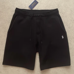 Ralph Lauren shorts - Storlek M . Pris lappen sitter kvar . Svarta shorts från Polo Ralph Lauren med klassisk broderad logga i vitt på ena benet. Modellen har snörning i midjan och är tillverkad i mjuk bomull, perfekt för en avslappnad och stilren look. Snygga fickor på sidorna och bekväm passform. Endast testade nån gång. Hör av vid fler funderingar 