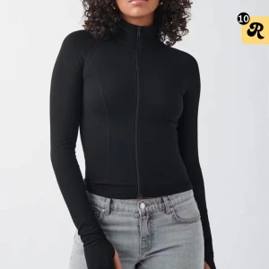 Svart slim långärmad ziptröja - Svart långärmad tröja med slim passform och hel dragkedja framtill. Hög krage och tumhål vid ärmsluten ger en sportig vibe. Perfekt att styla med jeans eller träningsbyxor. Materialet känns stretchigt och följsamt.