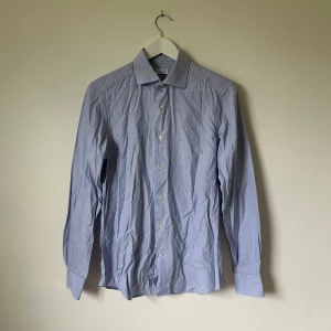 Blårandig skjorta från A Day's March - Klassisk blårandig skjorta från A Day's March med custom fit. Skjortan har lång ärm, knappar framtill och krage. Tillverkad i bomull och passar perfekt till jeans eller chinos. Snygg och stilren med diskreta smala ränder.  -  Artnr: A328