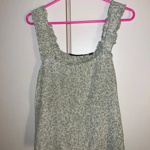 Grönmönstrad linnetopp från Vero Moda - Luftig linnetopp från Vero Moda i ljusgrönt och vitt med breda, rynkade axelband. Toppen har ett abstrakt mönster och är perfekt för varma dagar. Snygg att styla med jeans eller shorts för en chill look.