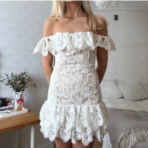 Vit spetsklänning  - Superfin kort vit klänning med offshoulder och volangkant. Klänningen har ett romantiskt spetsmönster och figurnära passform med volang nertill. (Har även denna i storlek S så skriv om ni hellre vill ha den)💞