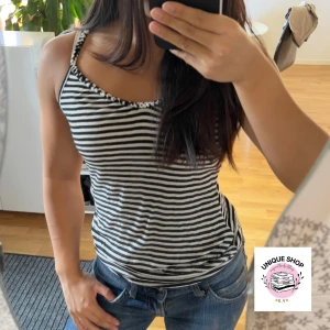 Randig svartvit linnetopp - Snygg randig linnetopp i svart och vitt med smala axelband och lätt rynkad kant vid urringningen. Perfekt för varma dagar och enkel att matcha med jeans eller shorts. Toppens material känns mjukt och följsamt mot huden.