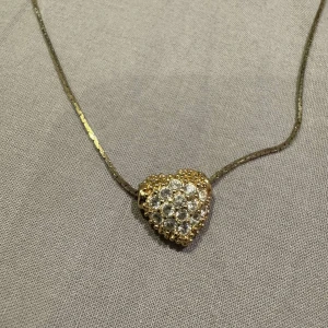 Guldigt halsband med hjärthänge - Superfint halsband med ett hjärtformat hänge täckt av glittrande stenar. Kedjan är tunn och elegant, och hänget har en lyxig känsla med sina gnistrande detaljer. Perfekt för dig som vill sticka ut med något extra sött och glammigt 😍